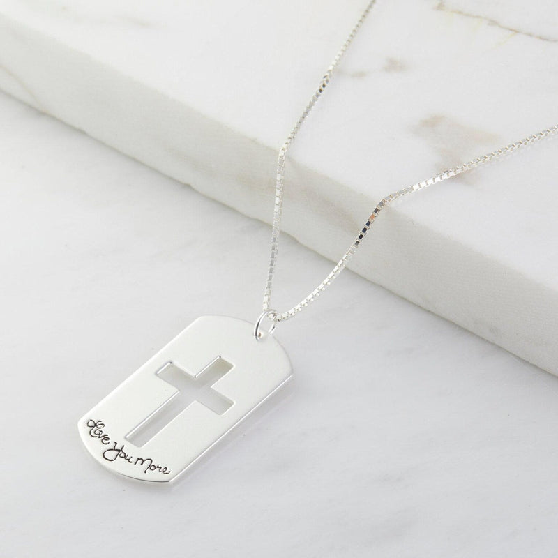Silver necklace with a dog tag pendant featuring a cross and engraved text on a marble surface.