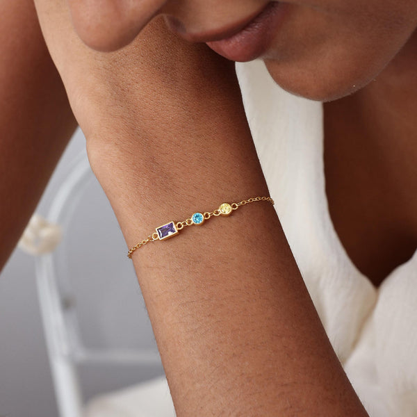 Gold bracelet with colorful stones on a wrist against a neutral background